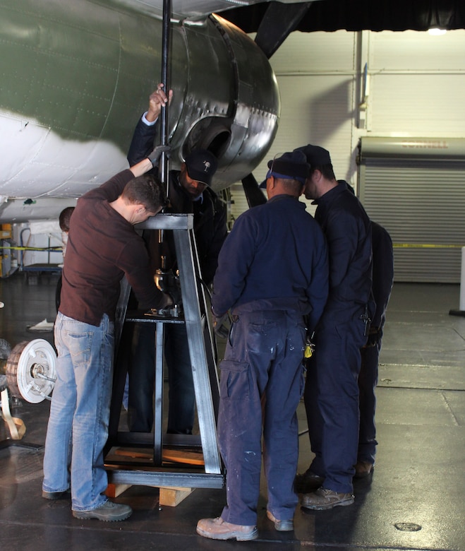 Tech. Sgt. Nathon Andrews (center) and members from Patriots Point maintenance staff, place a tripod jack under the wing of a B-25 bomber located at Patriots Point Maritime Museum in Mount Pleasant, S.C., to facilitate removing the wheel and tire assembly.