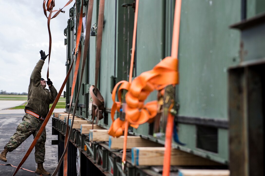 An airman throws a strap over a trailer.