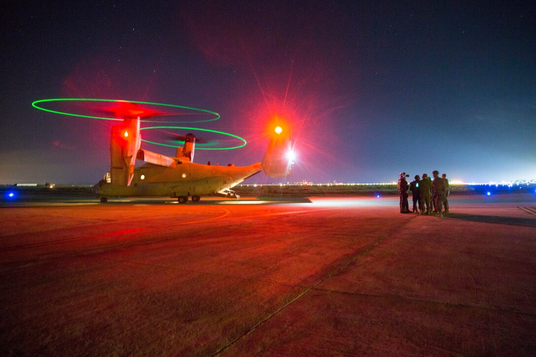 A military plane sits on the tarmac with its lights on at night.