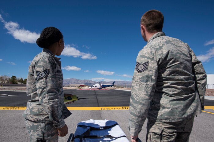 Two Airmen watch as a helicopter lands.