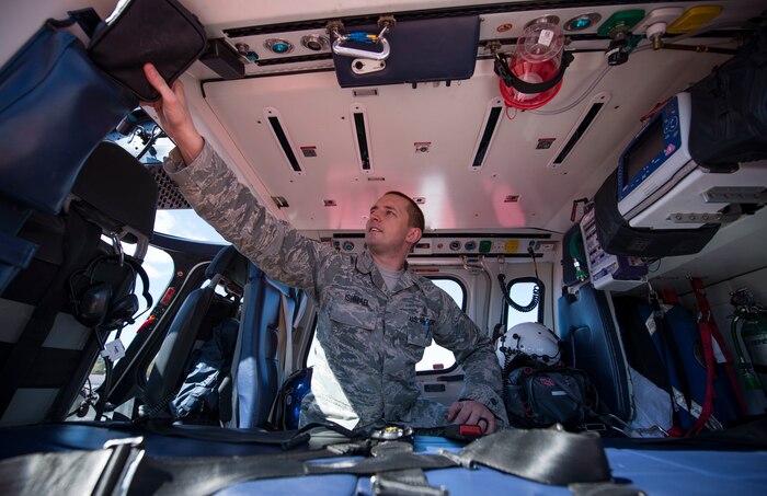 An Airman reaches for medical equipment inside of a helicopter.
