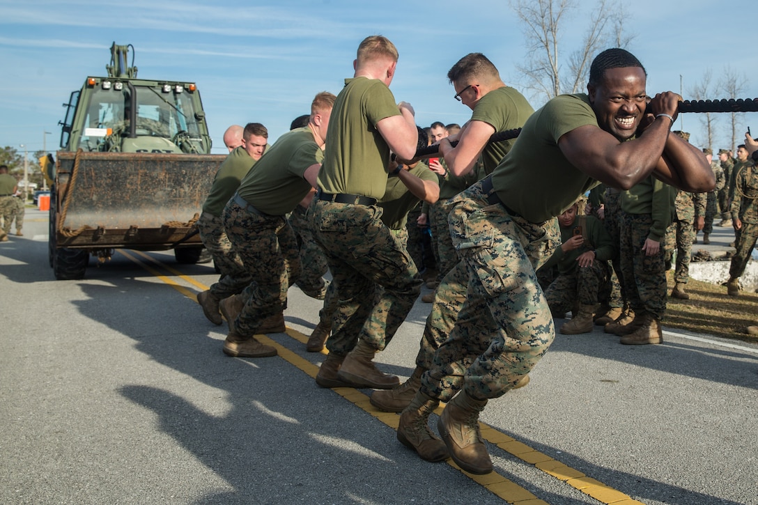 Marines pull a backhoe loader up a street.