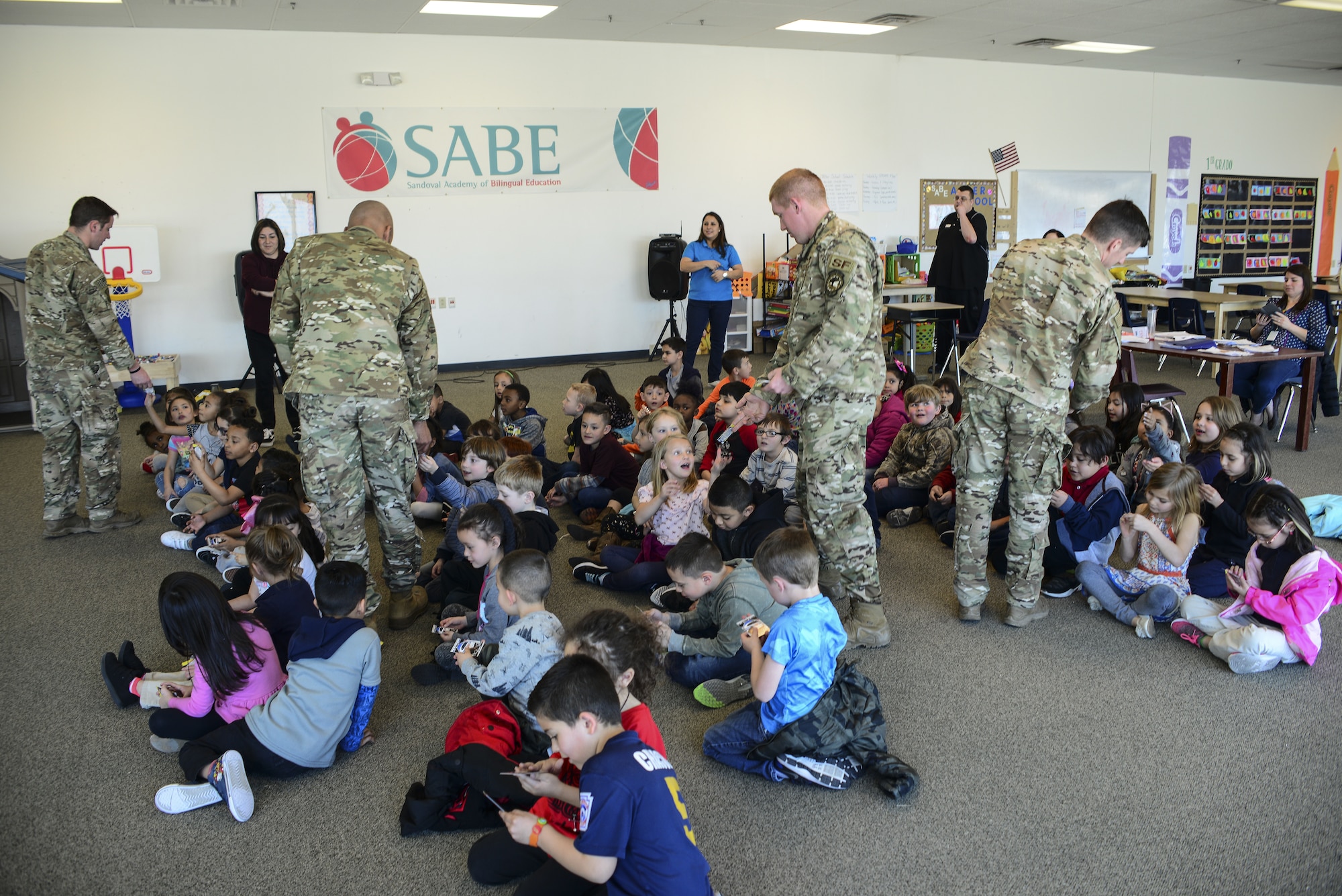 Members of the 377th Security Forces Squadron Military Working Dog section pass out playing cards to the students of the Sandoval Academy of Bilingual Education in Rio Rancho, N.M., March 15, 2019. The MWD team showed off some of the equipment they utilize to train the dogs such as the bite-suit and sound tactics. (U.S. Air Force photo by Staff Sgt. Kimberly Nagle)