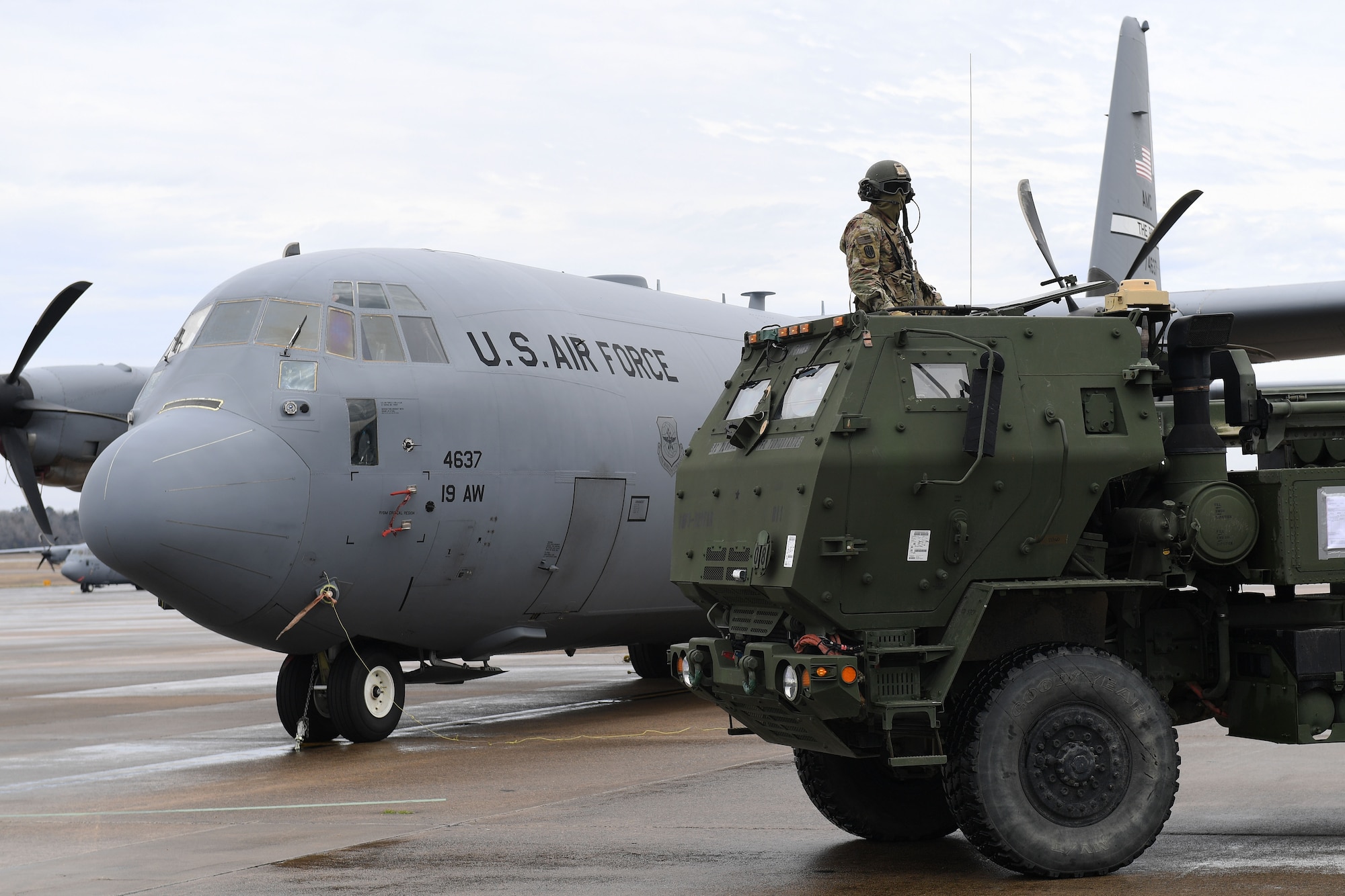 A man sits in a vehicle in front of a C-130J.