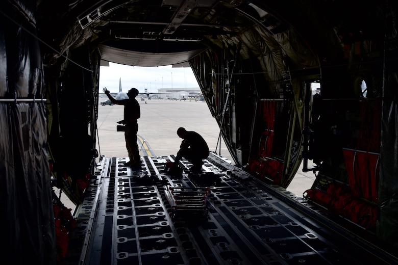 Two Airmen check the back of a C-130J.