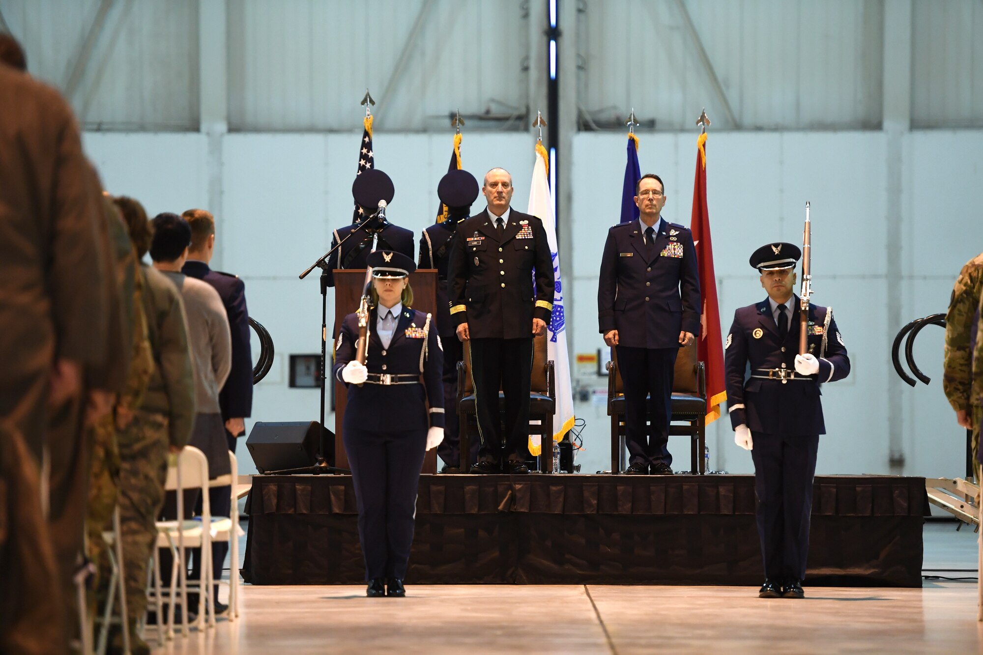 U.S. Army Maj. Gen. Gregory A. Lusk (left), the Adjutant General of North Carolina National Guard Bureau (NCNGB), and U.S. Air Force Col. Stephen J. Mallette (right), director of cyberspace operations for Joint Force Headquarters, NCNGB, stand at attention as members of 145th Force Support Squadron Honor Guard present the colors during Col. Mallette’s promotion ceremony at the North Carolina Air National Guard Base, Charlotte Douglas International Airport, Mar. 09, 2019. Family, friends, and guard members gather to watch Col. Mallette pin on the rank of Brig. Gen. He has has served for 37 years including enlisted time in the Army and Air Force.