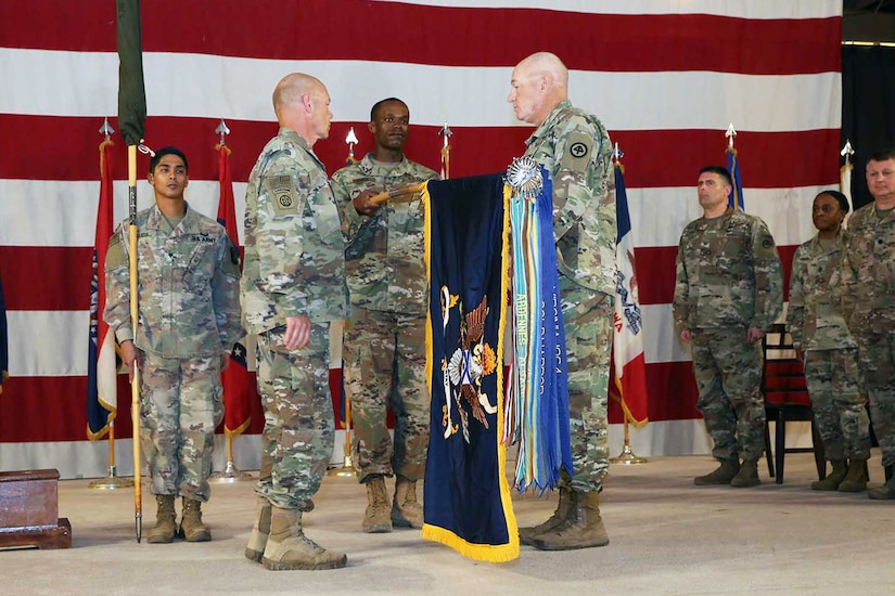 Lt. Col. Kevin Welsh (second from left), the battalion commander, and Command Sgt. Maj. Paul Horan (fourth from the left), the battalion command sergeant major, formally unfurl the 1st Battalion, 114th Infantry Regiment's flag signifying their unit's assumption of authority for security at Camp As Sayliyah, Qatar.