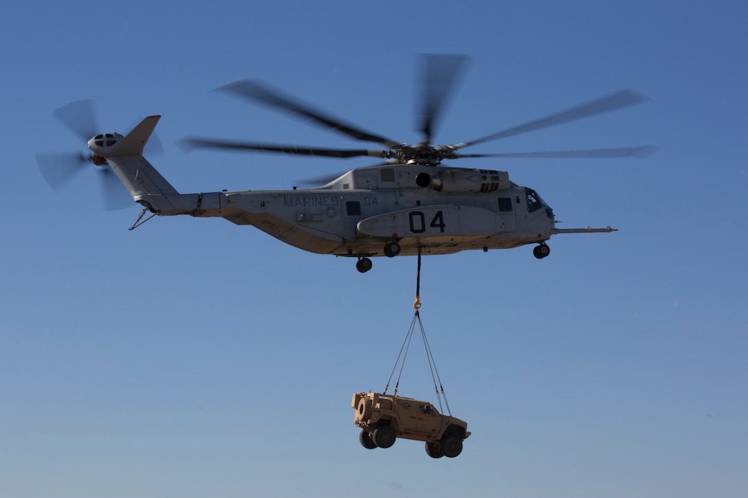 A helicopter carries a vehicle in a sling load.