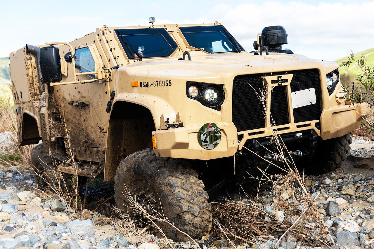 A tactical vehicle drives in sandy and rocky terrain.