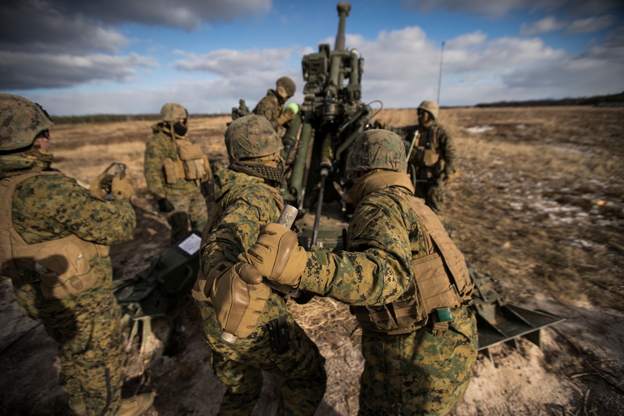 Uniformed service members load a large gun.