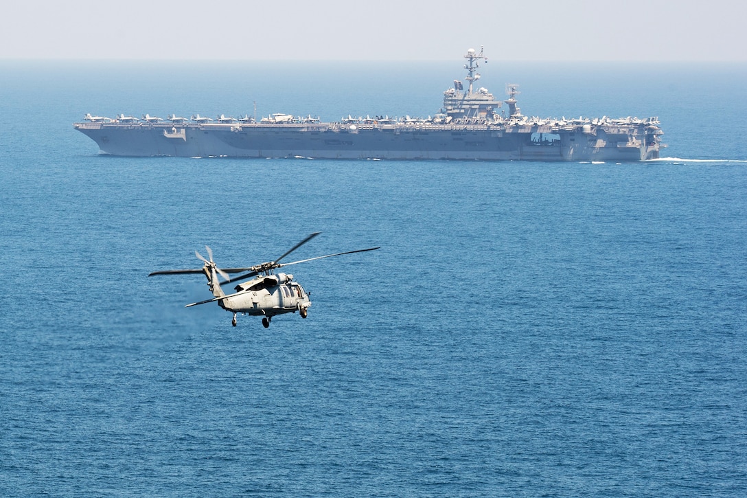 A helicopter flies toward an aircraft carrier.
