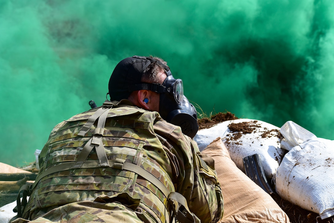 A soldier wearing a gas mask lies behind a haze of green smoke.