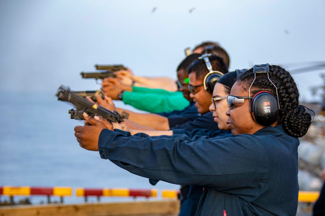 A group of sailors standing in a row fire guns.