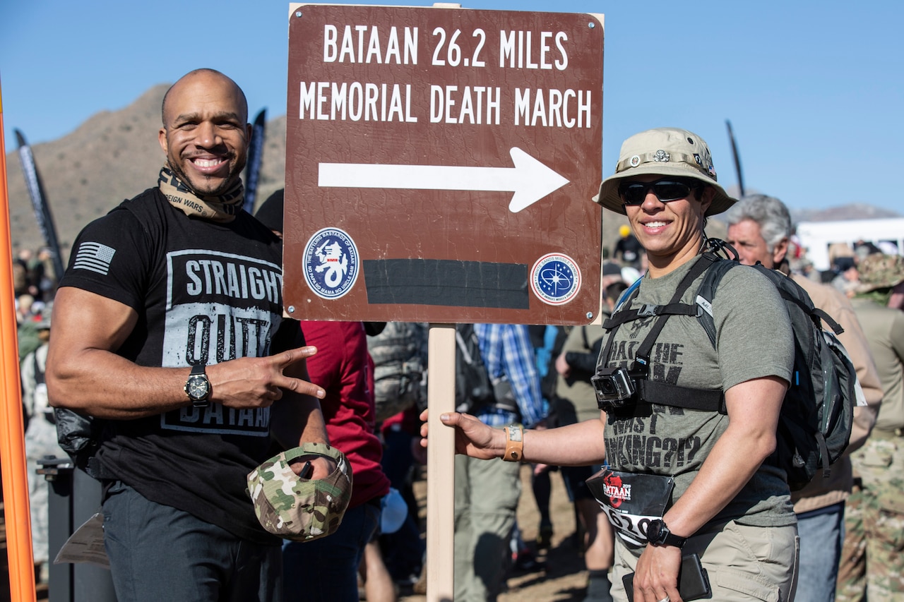 A man and woman pose for a photo with a sign reading “Bataan 26.2 Memorial Death March.”