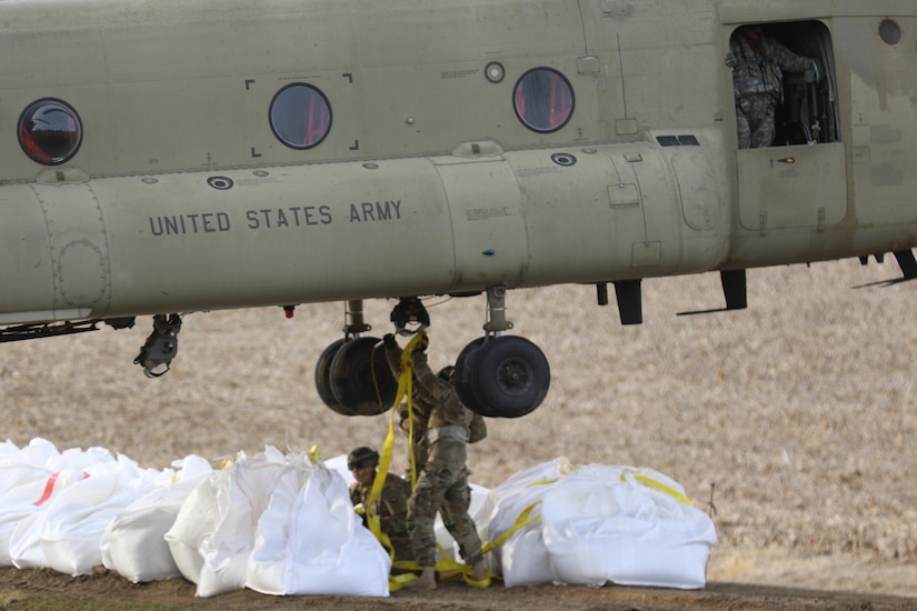 National Guard members attach sandbags to be carried by a helicopter in slings.