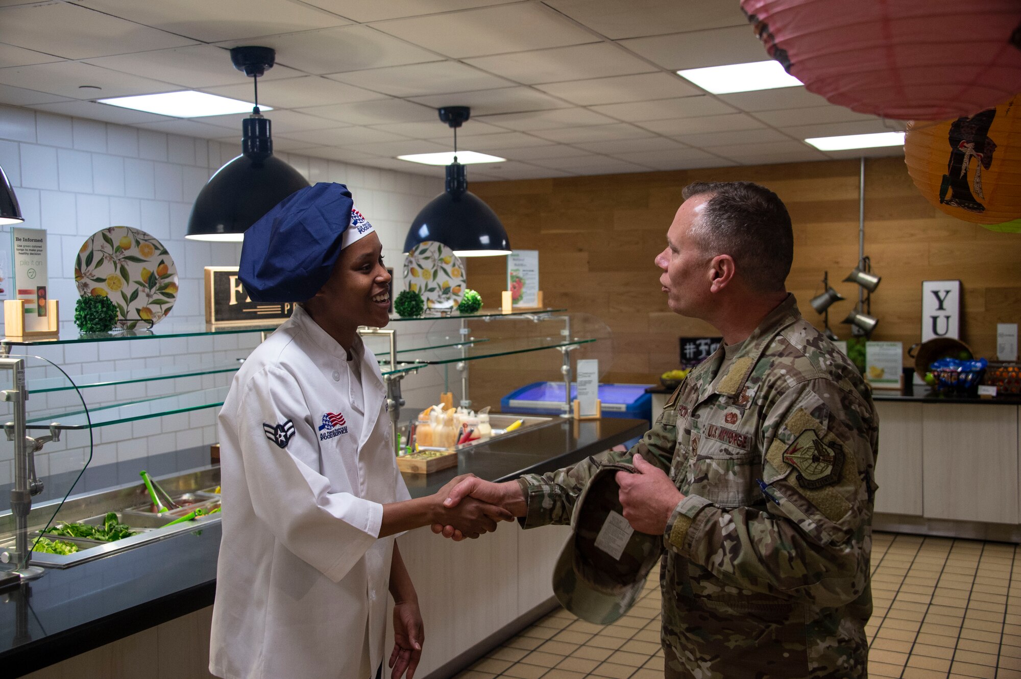 U.S. Air Force Airman 1st Class Kianna Randle-Traylor, a food services apprentice assigned to the 97th Force Support Squadron, shakes the hand of Chief Master Sgt. Erik Thompson, command chief of the 19th Air Force, during a tour of the dining facility,