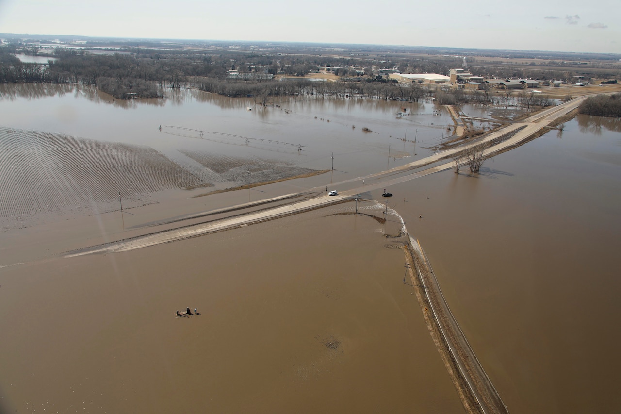 An aerial view shows a vehicle stranded on a road partially submerged under brown floodwater.