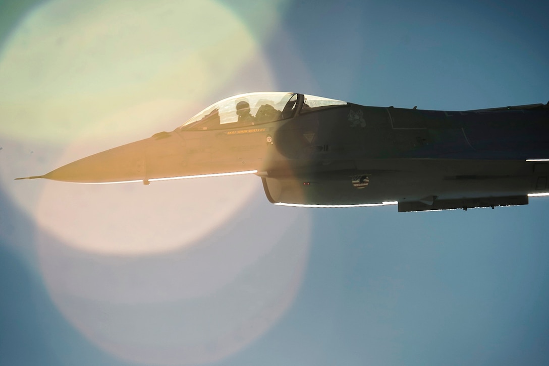 A military jet flies in a sunny blue sky.