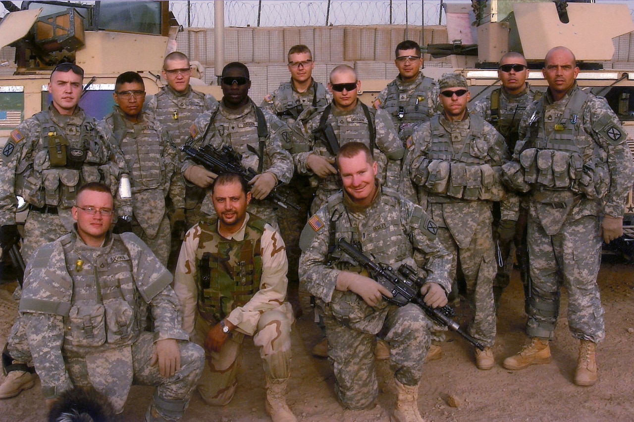 Several soldiers, some with guns, stand together on a dusty base.