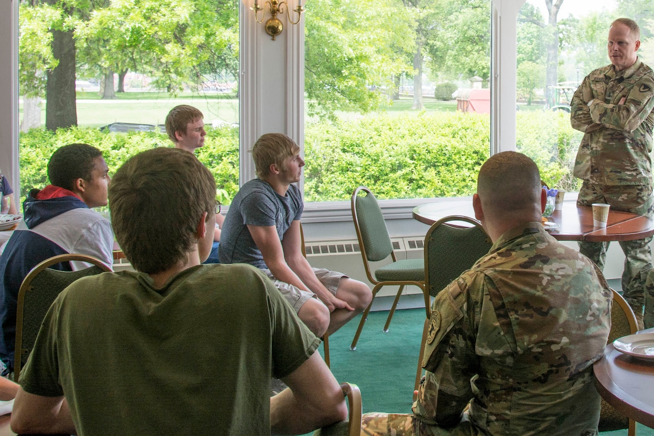 A soldier in a camouflage uniform speaks to a group of high school students.