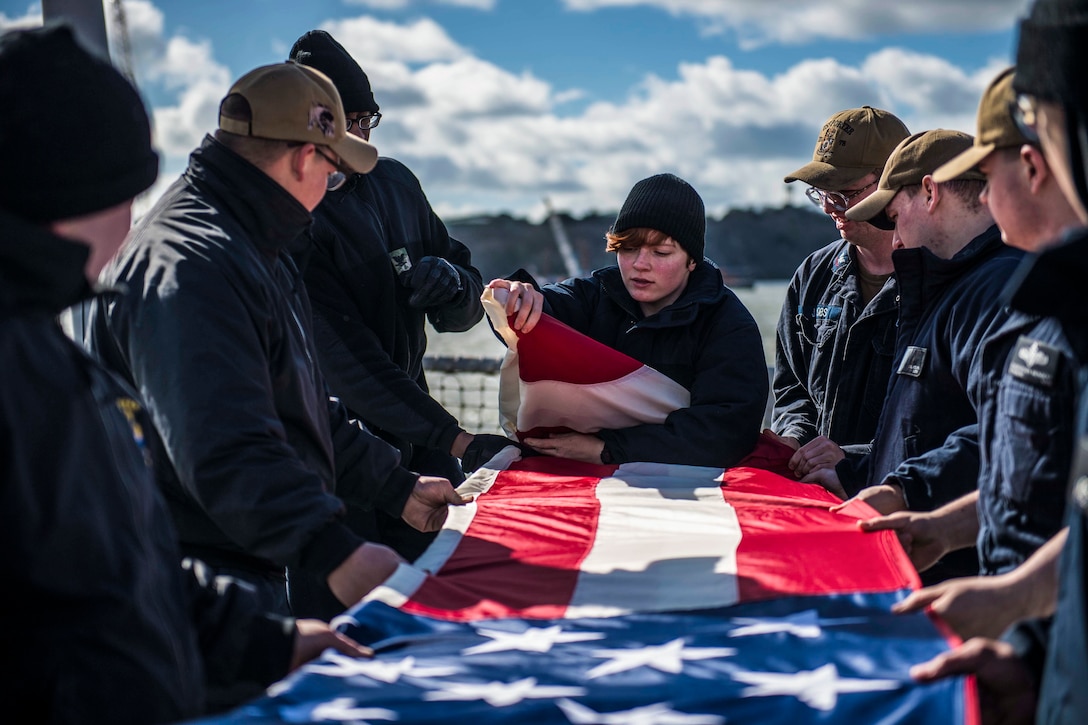 A group of sailors fold an American flag.