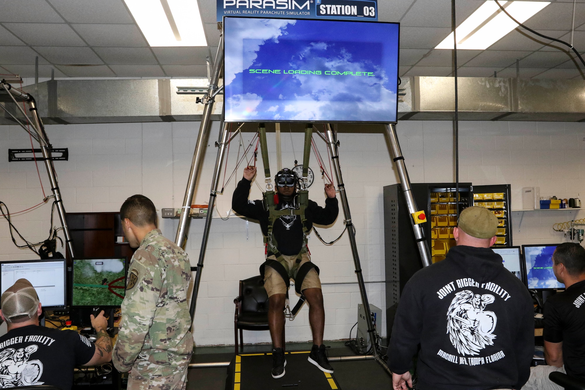 A paratrooper prepares for a virtual reality jump on the new Parachute Simulator (PARASIM) 7 as jumpmasters prepare a training scenario for him at the Joint Riggers Facility, MacDill Air Force Base, Tampa, Fla., Feb. 21, 2019. The PARASIM 7 recreates the experience of a real parachute jump from the head-mounted 3D virtual reality display to the suspension harness that detects jumper inputs. The physics-based parachute simulation technology recreates the conditions of a live jump using real-world scenes, malfunctions, wind profiles, various weather conditions and a full library of terrain types. (U.S. Army photo by Staff Sgt. Steven Colvin)