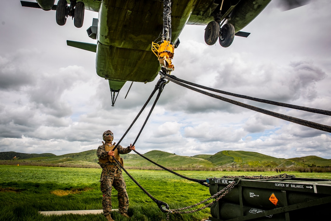 A Marine pulls two ropes hanging from a helicopter flying above.