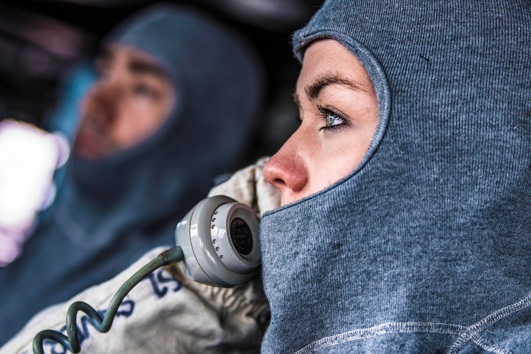 A sailor holds a phone up to her ear while staring into the distance.