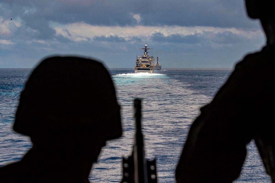 Two sailors look at two ships moving in the ocean waters.