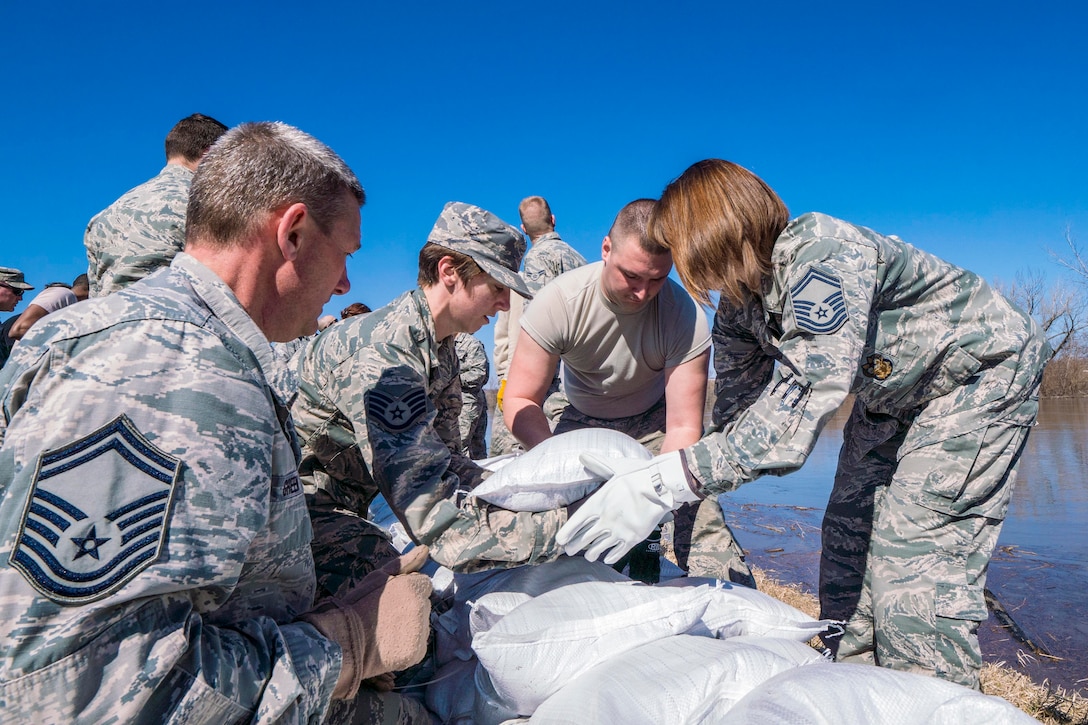 A group of airmen lay sand bags along a levee.