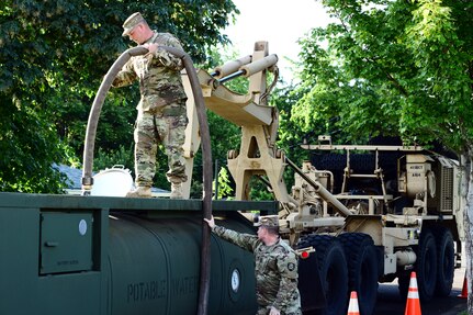 Oregon Army National Guard Soldiers, Sgt. 1st Class Lucas Thomas and Master Sgt. Christian Watts (below), use water from a fire hydrant in Keizer, Oregon, May 31, 2018, to fill a Load Handling System truck (M1120A4) compatible with 2,000-gallon water tank racks known as 'Hippos.' Similar vehicles are being used at the Pine Ridge Reservation to provide drinking water.