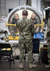 PANAMA CITY, Florida – Research Physiologist Lt. Travis Doggett, center, directs aircrew via radio during simulated flight in the Fluctuating Altitude Simulation Technology (FAST) system Jan. 14, 2019 at Navy Experimental Diving Unit. The system was developed and built by Naval Surface Warfare Center Panama City Division.