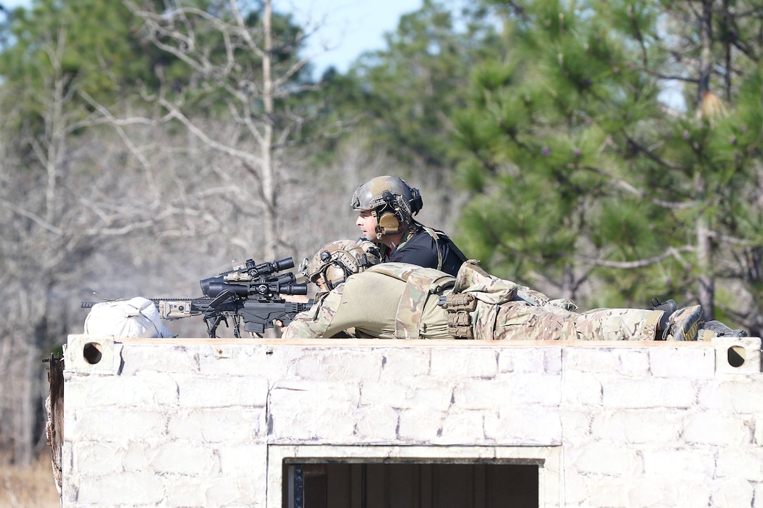 A service member aims a weapon on a roof.