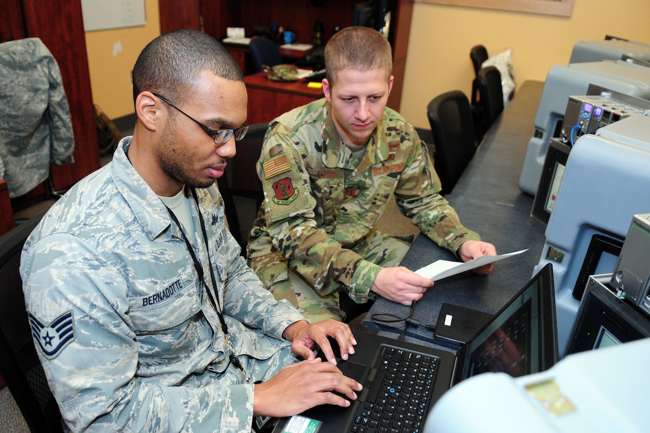 Two uniformed men look at a computer.