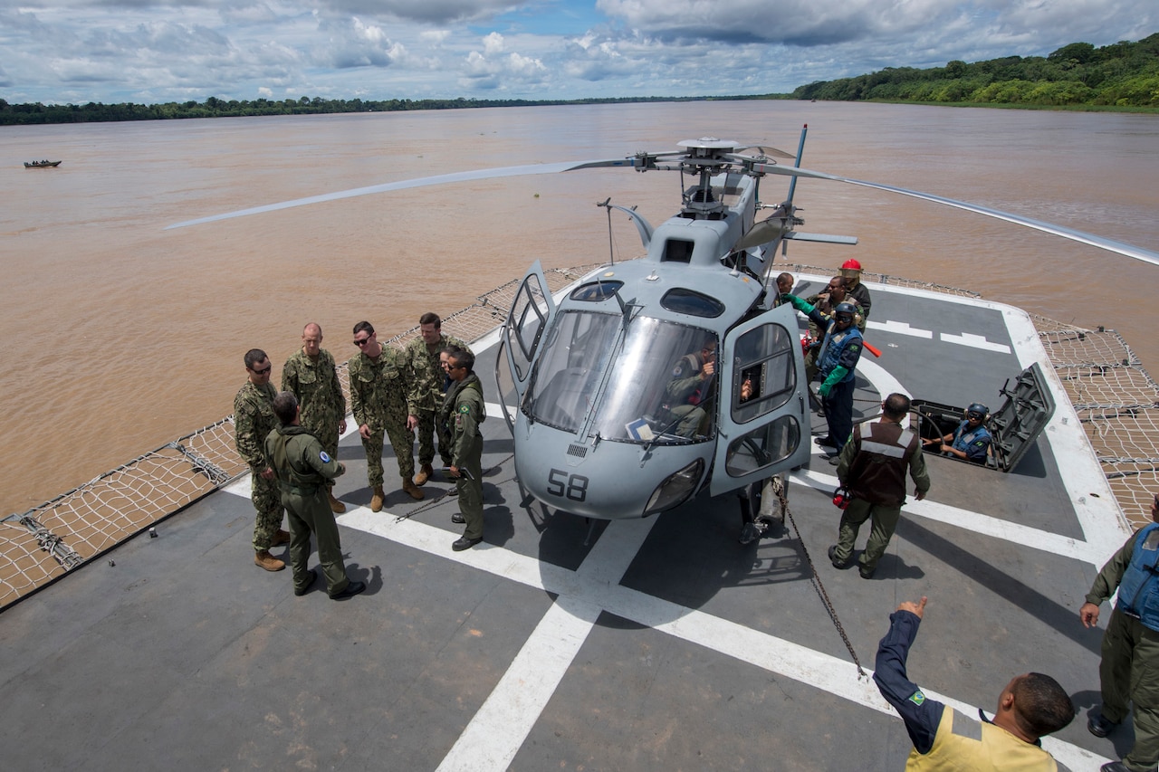 Sailors huddle near helicopter on ship.