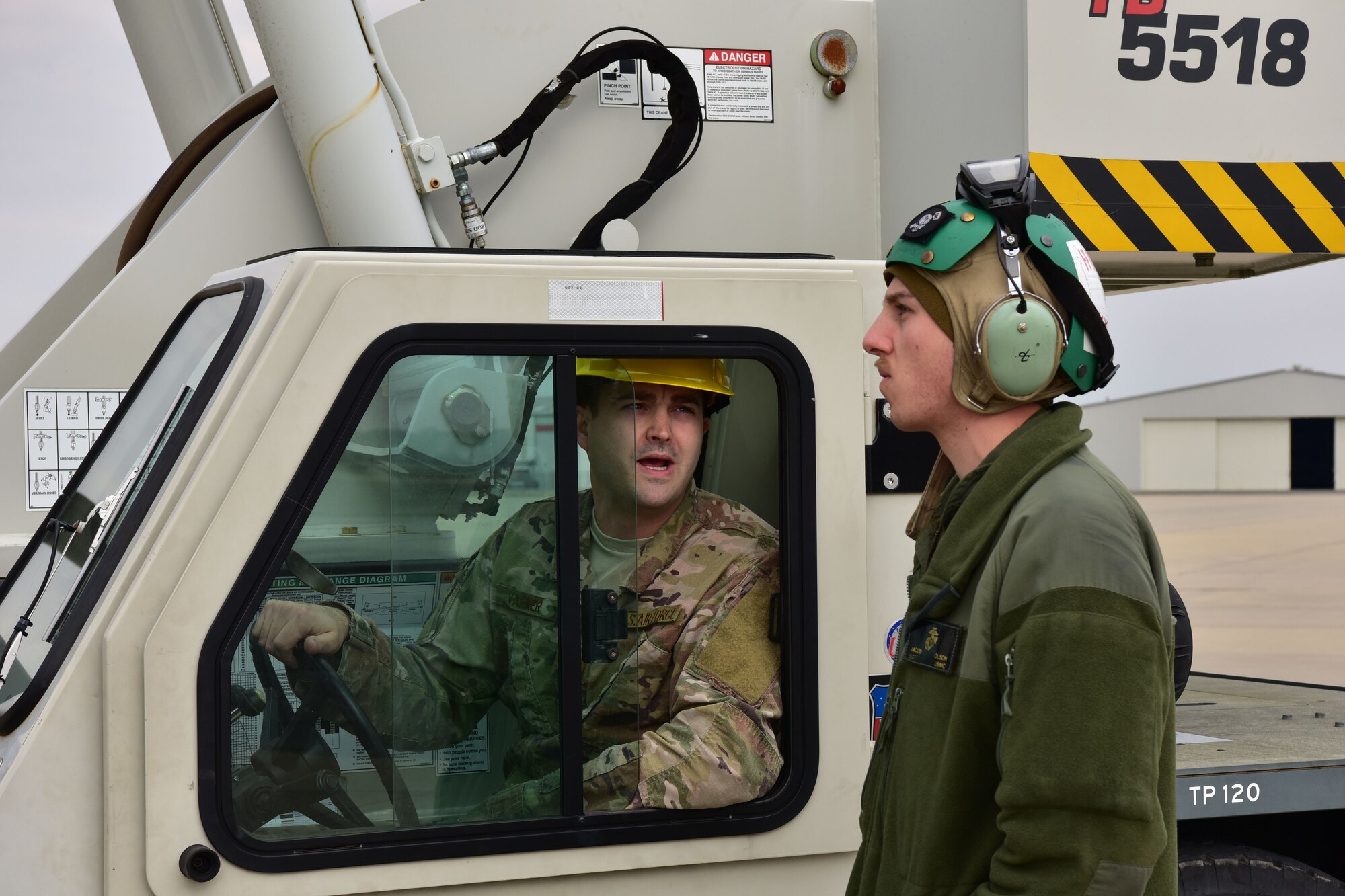 A man in the operational camouflage uniform in a crane speaks to a man in a flight suit and a headset.