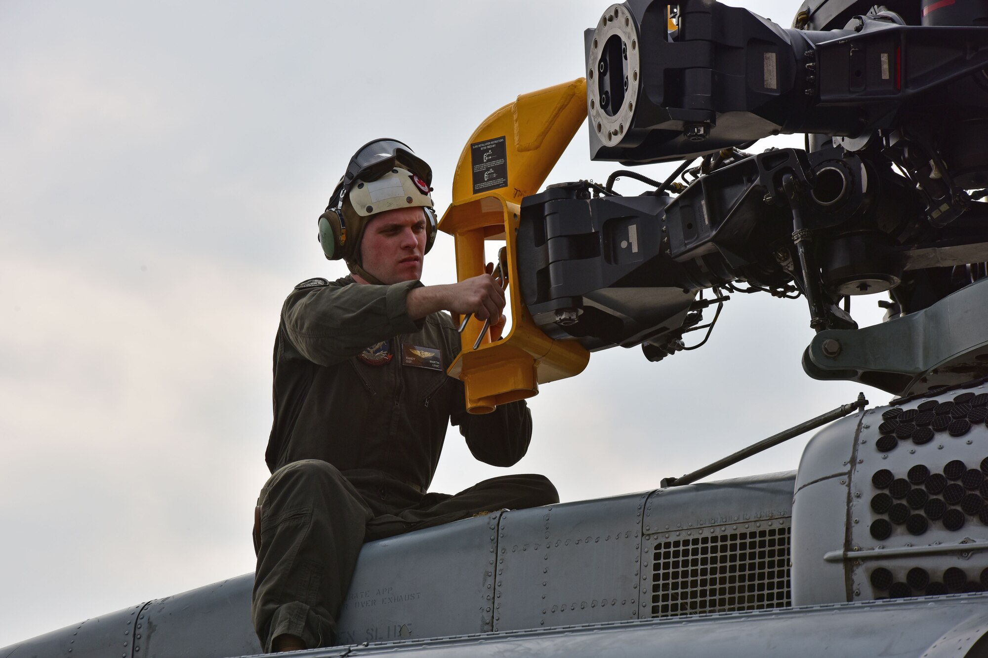 A man wearing a flight suit holds part of a helicopter rotor.