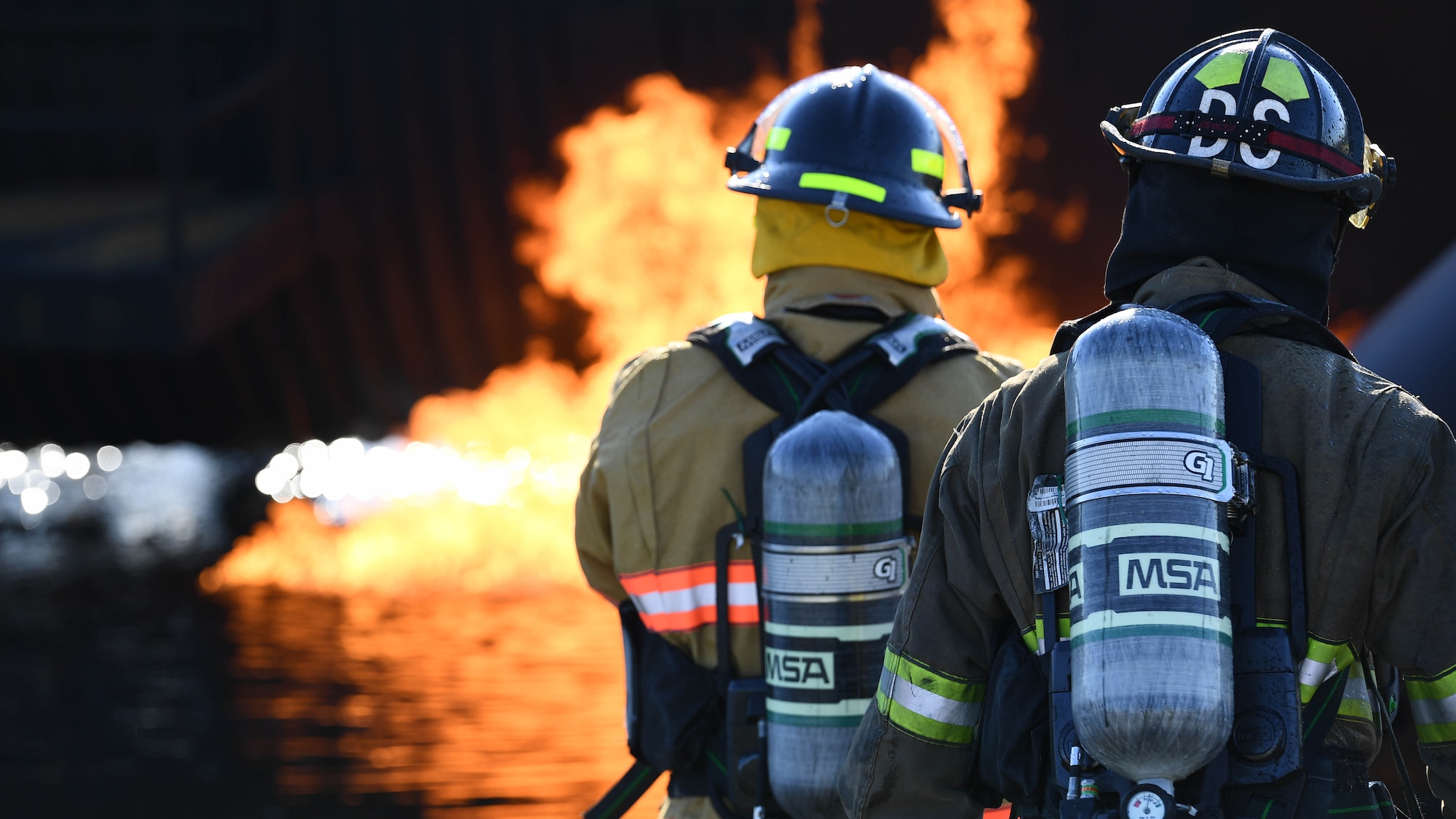 Shreveport Fire Department firefighters look at a simulated aircraft fire March 21, 2019, at Barksdale Air Force Base, Louisiana. Underground gas pipes are used to pump fuel into the simulation aircraft and ignite it on fire. (U.S. Air Force photo by Airman Jacob B. Wrightsman)