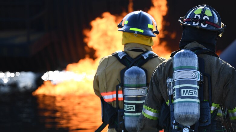 Shreveport Fire Department firefighters look at a simulated aircraft fire March 21, 2019, at Barksdale Air Force Base, Louisiana. Underground gas pipes are used to pump fuel into the simulation aircraft and ignite it on fire. (U.S. Air Force photo by Airman Jacob B. Wrightsman)