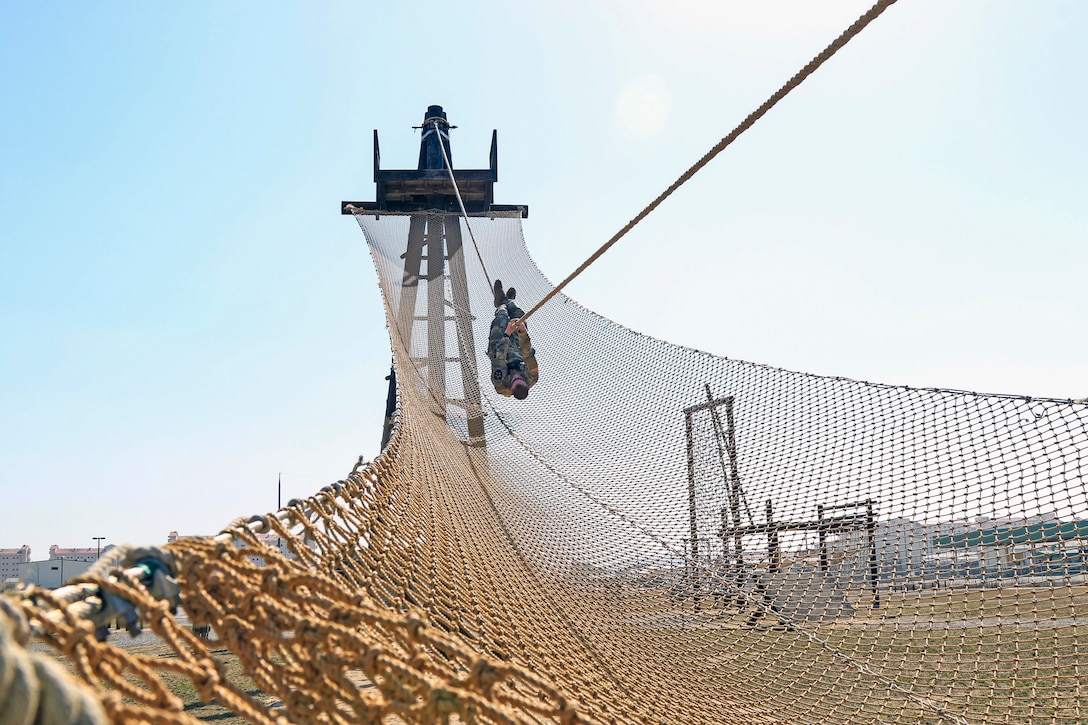 A soldier hanging upside down slides down a rope.