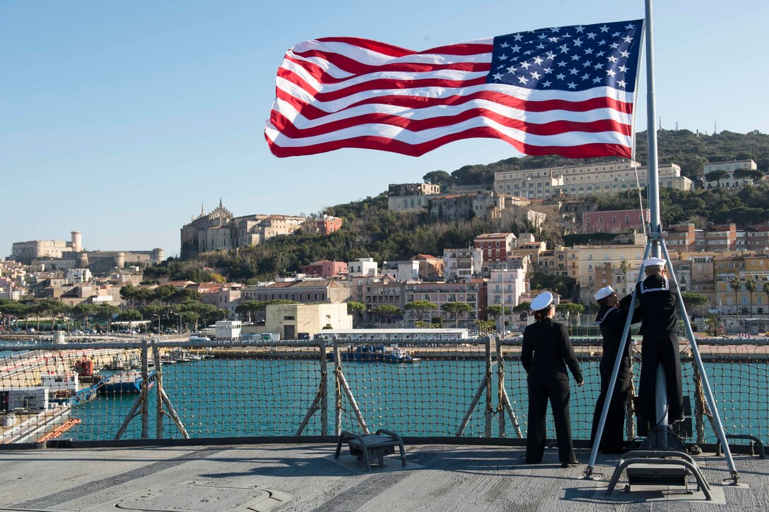 Three sailors raise an American flag.