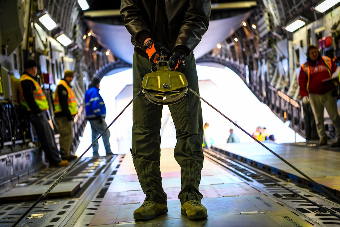 An airman inside an aircraft pulls a rope with four other people standing in the background.