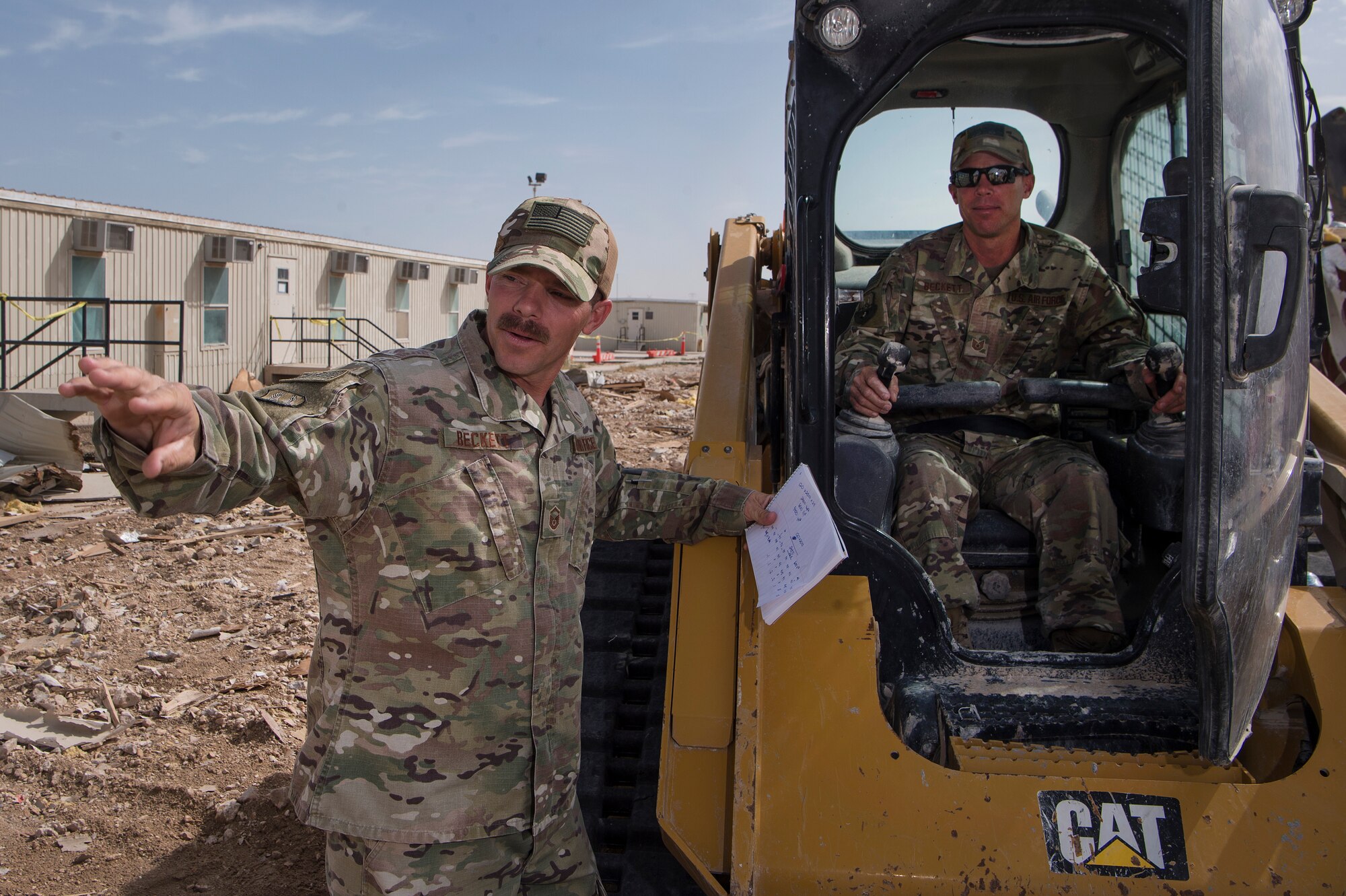 Master Sgt. Christopher Beckett, left, 379th Expeditionary Civil Engineer Squadron (ECES) heavy equipment section chief, and Tech. Sgt. John Beckett, right, 379th ECES heavy equipment project lead, work together at a construction site March 27, 2019, at Al Udeid Air Base, Qatar. The brothers, who have served in the Arizona Air National Guard since 2003, are currently deployed together to the same ECES unit at Al Udeid Air Base. (U.S. Air Force photo by Tech. Sgt. Christopher Hubenthal)