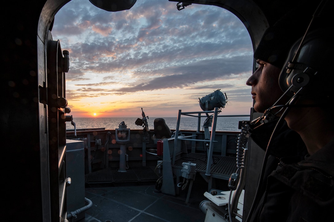 A service member stands watch on a boat.