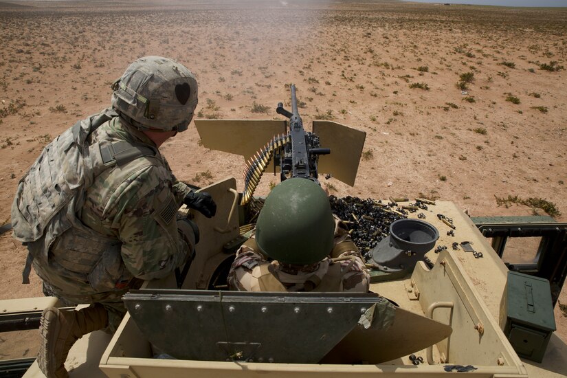 Two service members with their backs to the camera train on a machine gun.