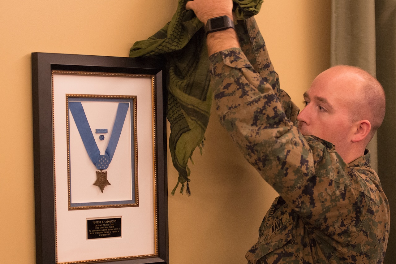 A Marine unveils a plaque on a wall that holds the Medal of Honor.