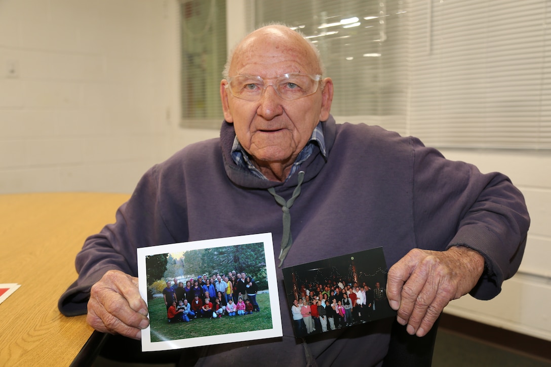 Telfinues Preszler, or Papa Tel, a heavy equipment mechanic, displays two photographs which he keeps at his work station, showing many of his children, grandchildren and great grandchildren, during an interview conducted at Production Plant Barstow, Marine Depot Maintenance Command, at the Yermo Annex aboard Marine Corps Logistics Base Barstow, Calif. He boasted that he had 10 children, 18 grandchildren, and 10 great grandchildren which he visits with when he is able to.