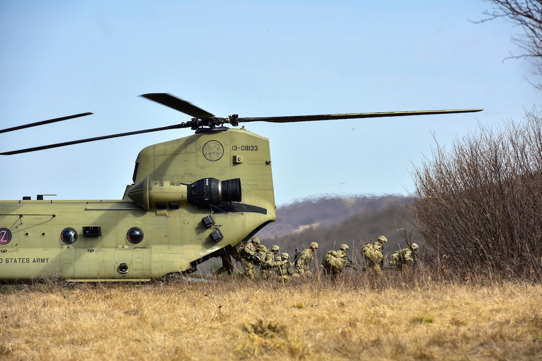 A group of soldiers exit a helicopter into a dry grassy field.