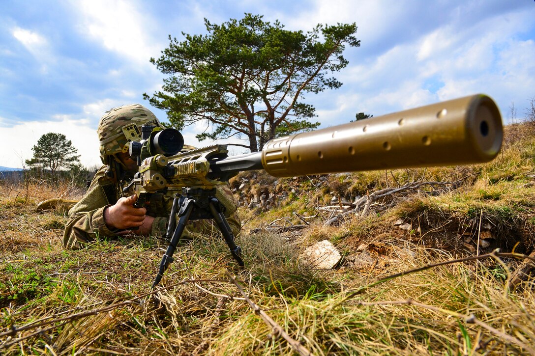 A soldier lies on a the ground pointing a weapon.