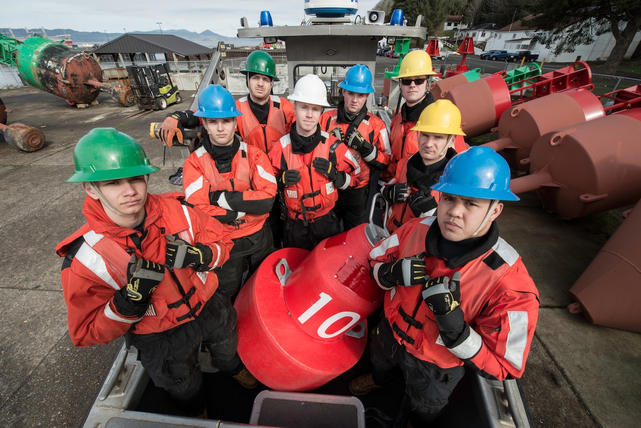 Eight Coast Guardsmen pose with an orange buoy.